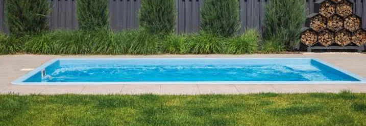 Ein Pool im Garten mit Rasenfläche und Sichtschutzzaun aus Metall.